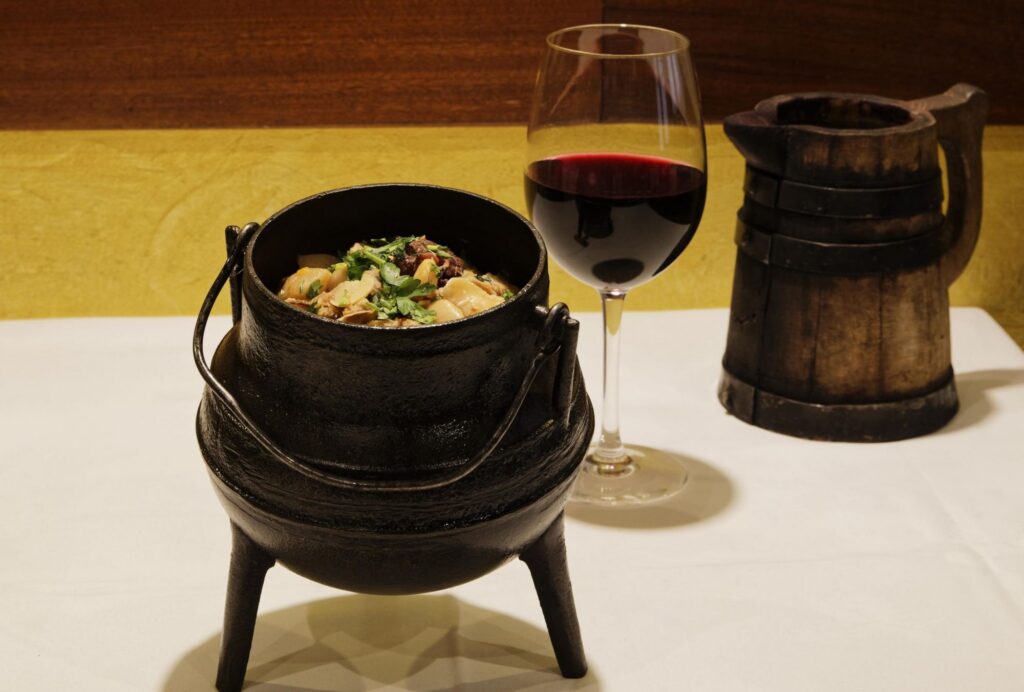Feijocas numa panela de ferro de três pés, com copo de vinho tinto e jarro de madeira