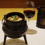 Feijocas numa panela de ferro de três pés, com copo de vinho tinto e jarro de madeira